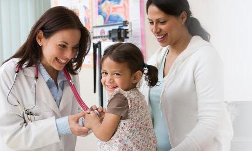 Pediatric nurse practitioner smiling taking heart rate of toddler patient